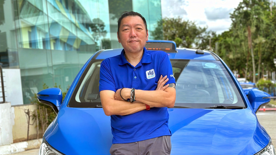 Ricky Low wearing a blue ComfortDelGro polo shirt and standing beside a blue ComfortDelGro taxi.