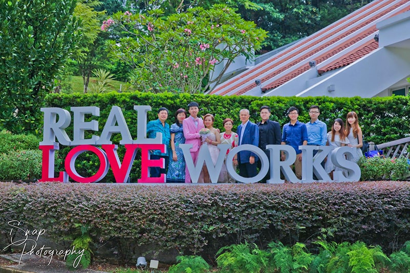 A family posing behind some big letter statues that read REAL LOVE WORKS